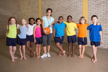 Cute pupils smiling at camera with PE teacher at the elementary school